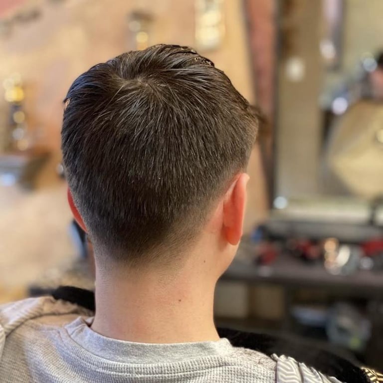 Back view of a person with short dark hair and a fade haircut, wearing a light gray shirt in an indoor setting