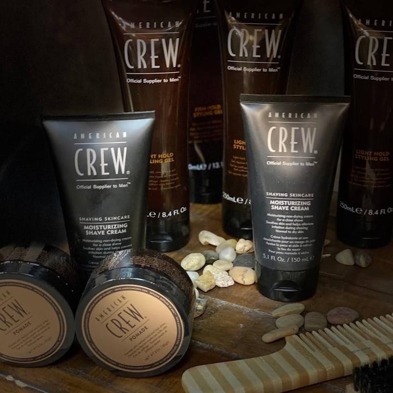 American Crew mens grooming products including shave cream, moisturizer, and other hair care items arranged on a wooden surface with a comb