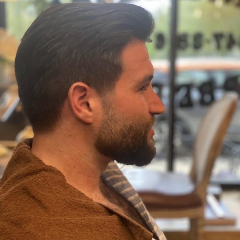 Profile view of a man with dark hair and beard wearing a brown shirt in an indoor setting