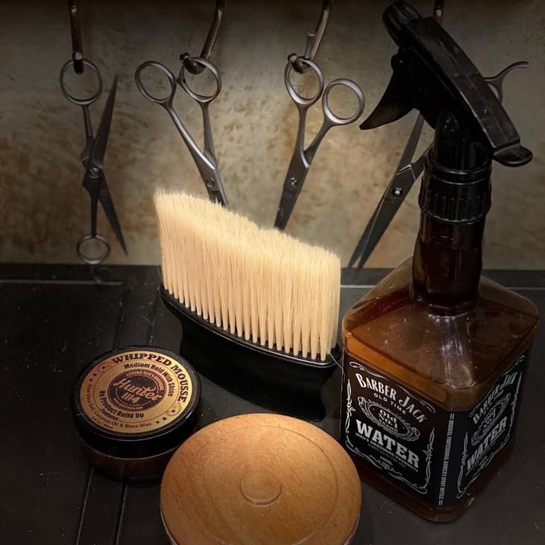 Barber tools displayed on black surface: scissors, comb, brush, spray bottle, and containers of grooming products
